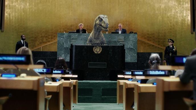 A United Nations panel with multiple people at desks with headsets, there is a velociraptor at the front of the room at a lecturn.