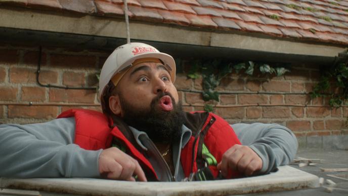 A Man wearing a hard hat is stuck in a hole in the roof.