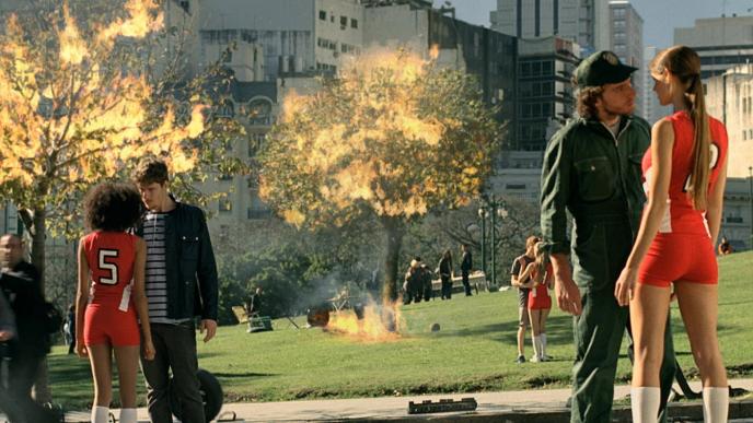 couples standing close to each other as trees are aflame and the city behind crashes