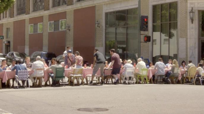A group of people sit at a long table in the road at an intersection