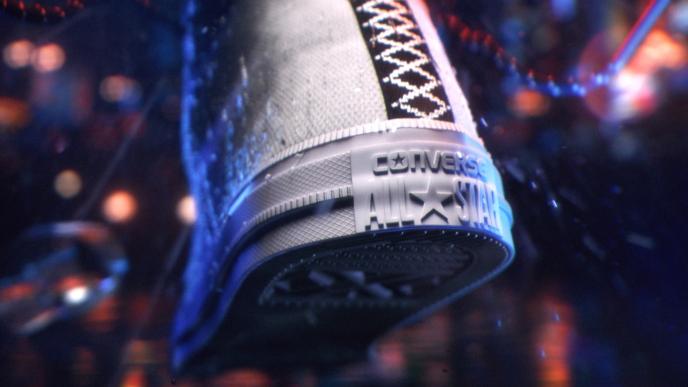 The back of a Converse trainer showing the logo and the underside of the shoe is splashing water. There are city lights in the background.
