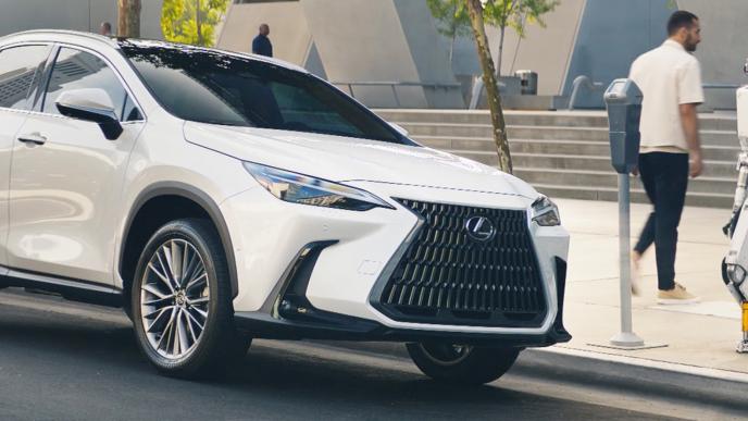 A man walks out of his white Lexus SUV that is parked at a parking meter. A white robot stands next to the car.