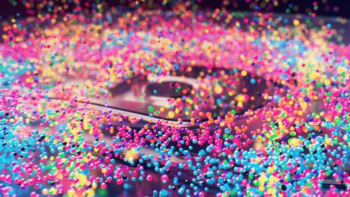 A speaker with multicoloured bubbles on it bouncing them up against a black background.
