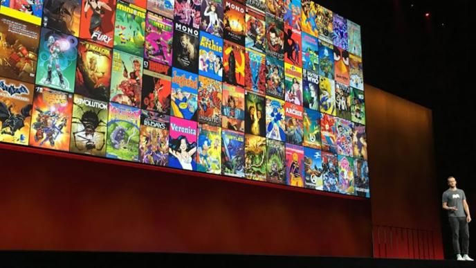 Man giving a talk on a stage in front of a wall of comic book covers