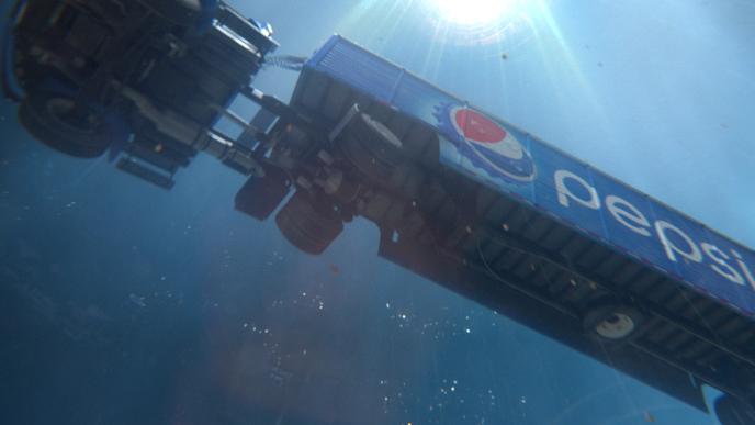 A Pepsi truck is floating through the air with a blue background and light overhead. 