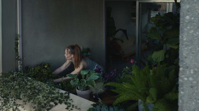 Concrete block of flats focusing on one balcony full of green plants with a girl watering the, 
