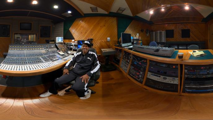A fish-eye view of a man sitting at a mixing desk in a recording studio.