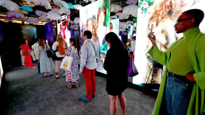 People stand in a line and take photos of Carrie Bradshaw (from 'Sex and the City') who is displayed on various screens