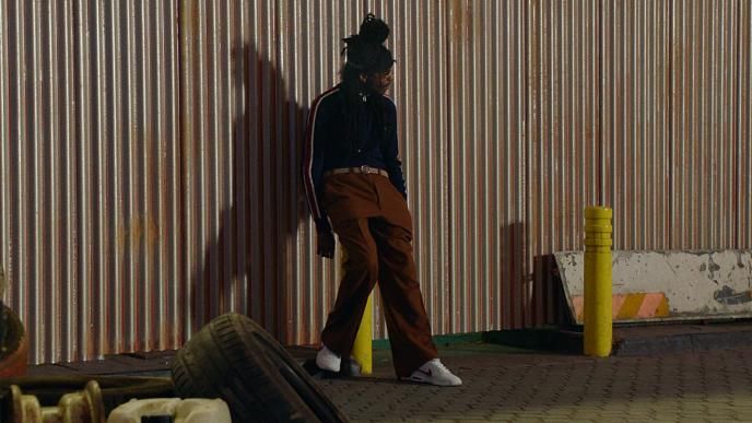 A man stands against a wall in an industrial part of town.