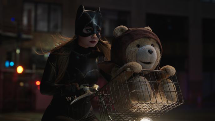 Ted sits in the basket on the front of a bicycle, being ridden by Blair, dressed as Catwoman
