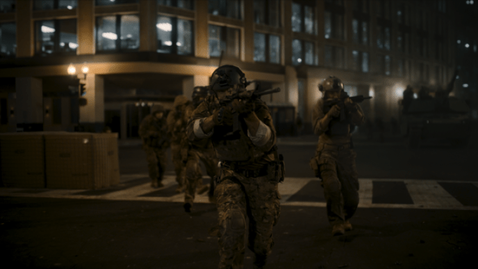 A group of armoured soldiers holding guns walking through a street.
