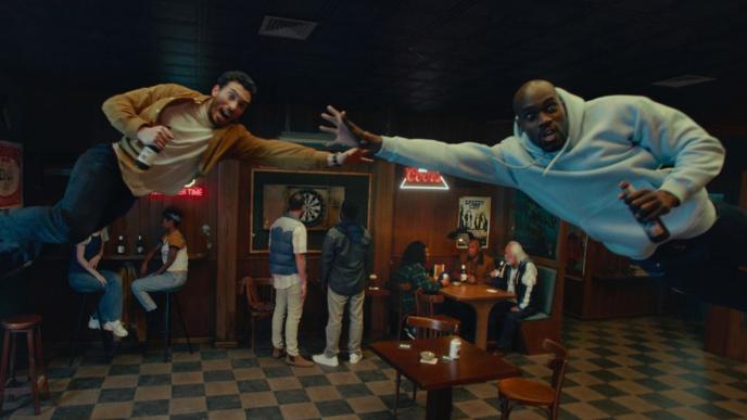 Two men in a bar in mid air reaching for a Coors Light