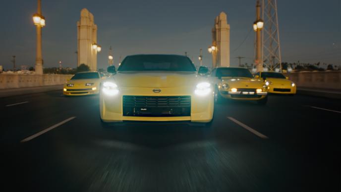 Four yellow Nissan Z vehicles drive across a bridge - each a different variation of the model
