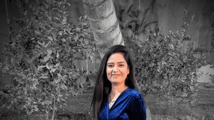 A woman wearing a blue dress standing in from of a hedge. 