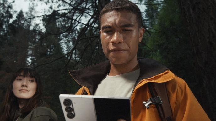 Two hikers, a man and a woman, in the woods. The man holds a Samsung Galaxy Z Fold6