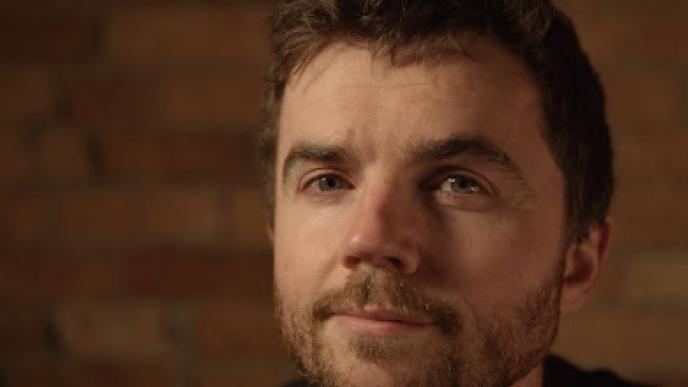 A headshot of a man in front of a brick wall.