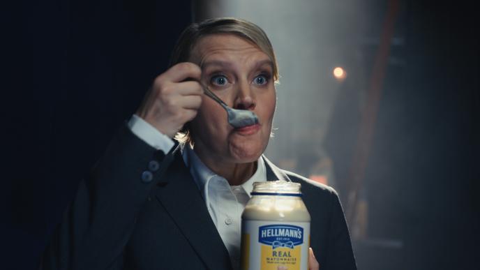 Actress Kate McKinnon on a stage in a suit eating mayonnaise from a jar