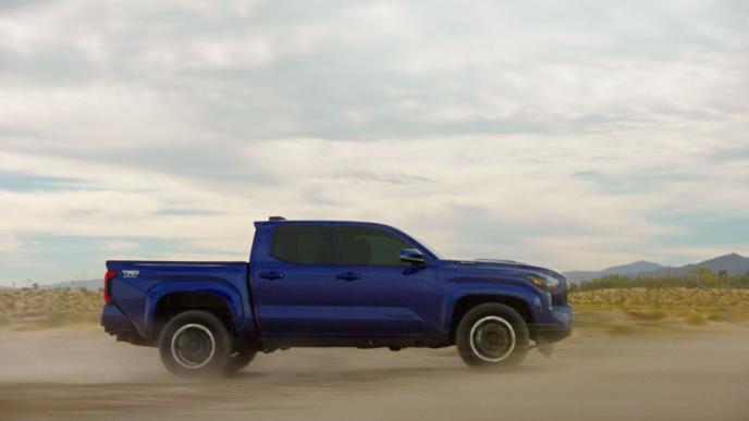 A blue Toyota Tacoma drives through the sand