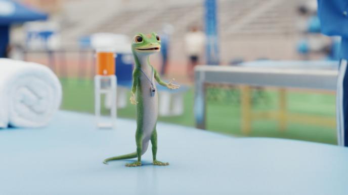 The animated GEICO Gecko stands on a training table on a football field