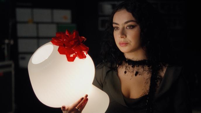 Charli xcx holds a lamp with a red bow on it