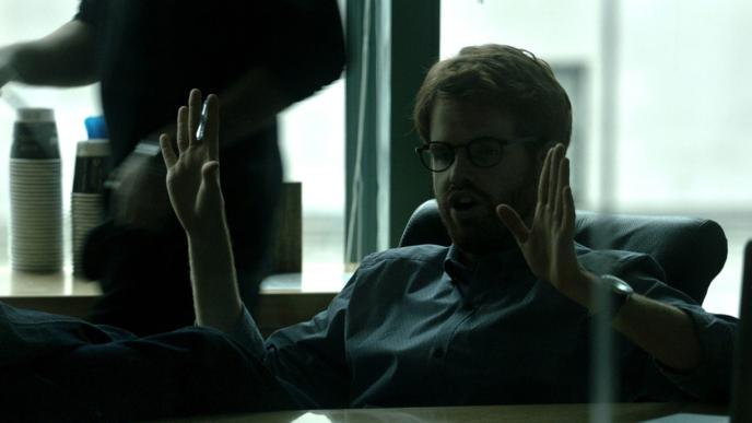 A man at a desk holds his hands up while on a conference call