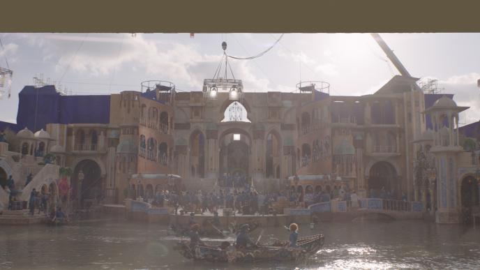 Plate footage from Wicked Part One, showing the front of Shiz University. Boats sit on a lake in front of an elaborate building facade set