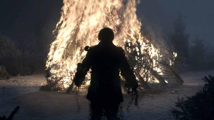 back view of scrooge from a christmas carol standing in front of a large burning bonfire