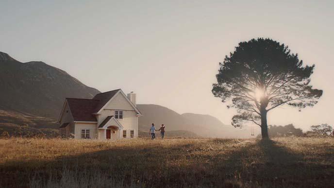 Still of landscape scene. A couple in a sunny field between a house and a large tree