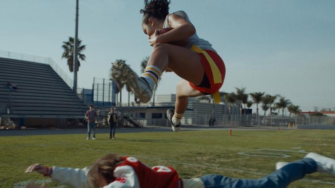A female flag football player jumps over a male competitor