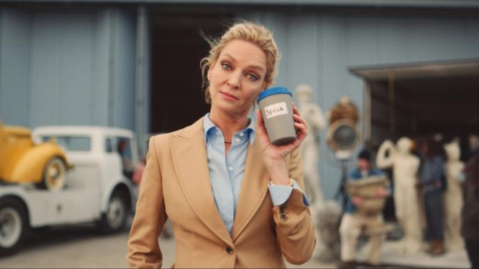 actress uma thurman raising eyebrows while holding a coffee cup that has 'spock' written on it in front of a film set