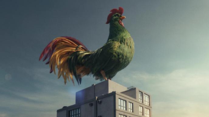 A large green CGI rooster sits on top of a tall urban building
