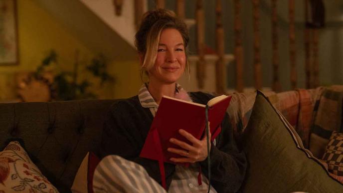 Still from Bridget Jones Mad About the Boy film. Bridget Jones sitting on sofa with a book