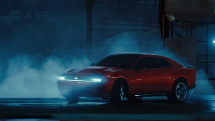 A red Dodge car drifts in an industrial parking lot