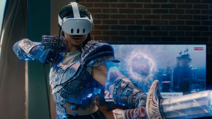 A woman in a living room wears warrior gear and a VR headshot and holds a sword