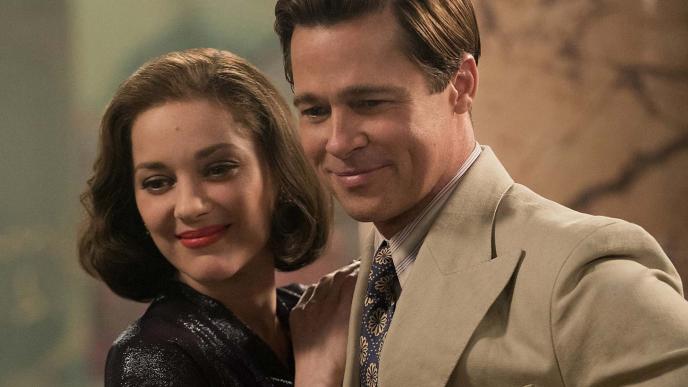 A man and a woman stand close together, both looking down. 