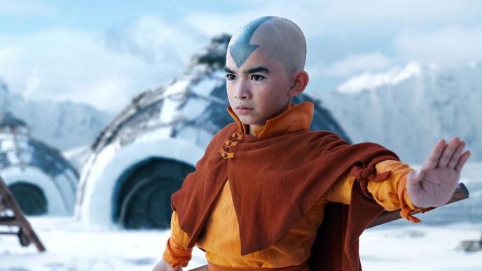 A young boy wearing orange robes, with a blue arrow painted on his shaved head, standing in a snowscape
