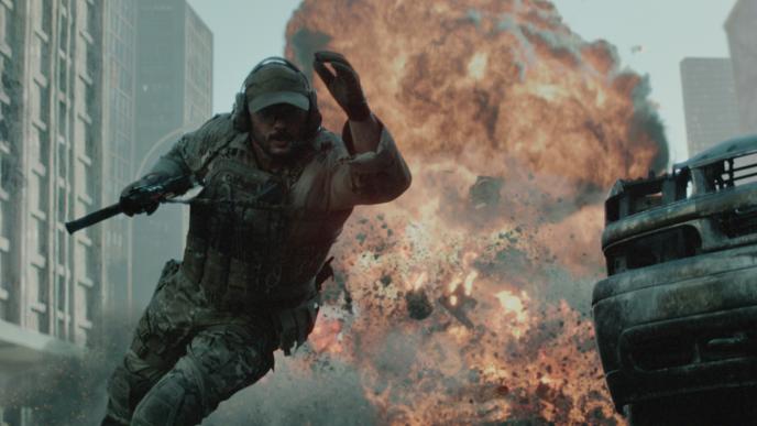 A soldier in tactical gear runs from a massive explosion in a city street, surrounded by debris and damaged vehicles.