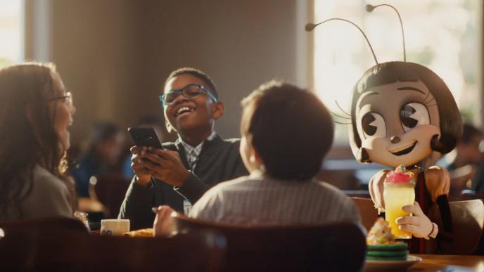 A character from the film IF sits at a table in an IHOP restaurant with a group of children in suits