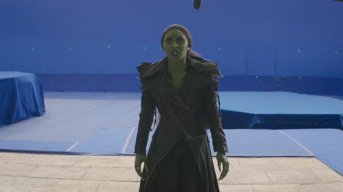 Cynthia Erivo as Elphaba in Wicked: For Good, walking up the steps of Shiz with a blue screen background