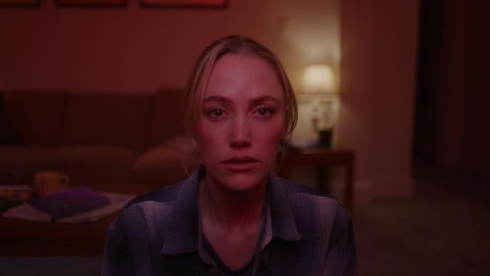 Actress Maika Monroe stares straight forward at a television in shock