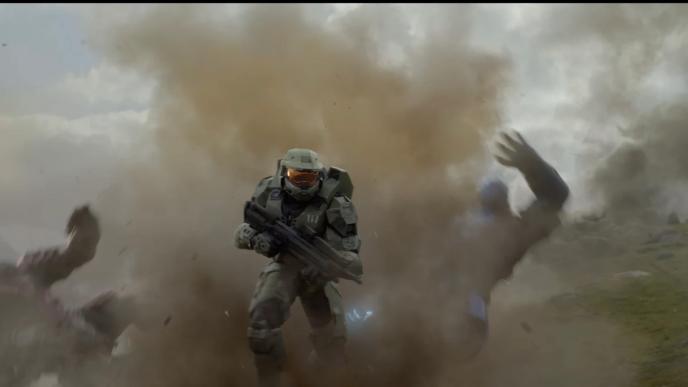 Armored futuristic soldier stands amid explosion, dust and debris flying, while two figures are thrown backward in a grassy landscape.