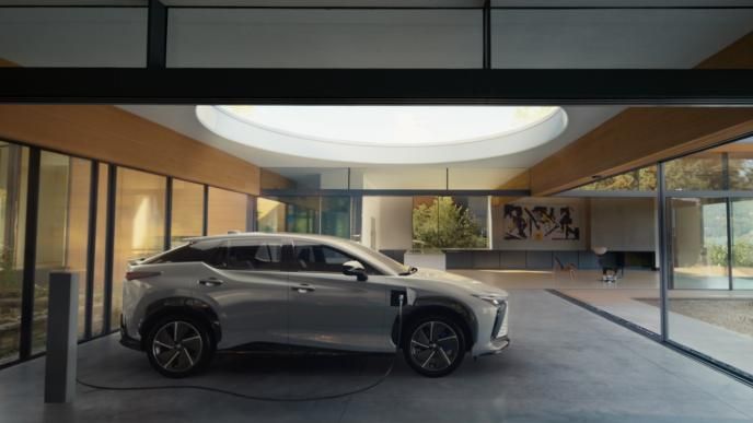 A white electric Lexus SUV charging inside a modern glass-walled home overlooking a serene lakeside landscape
