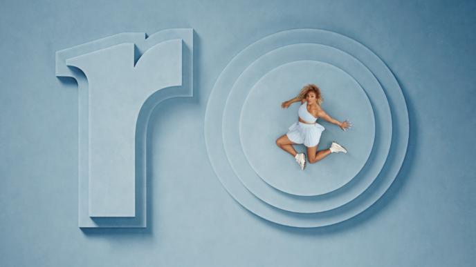 Serena Williams sits on a blue set with set pieces that say ro. She sits on the O