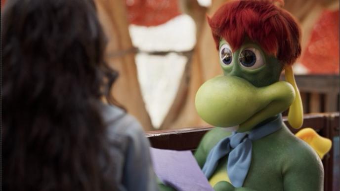 A still from an ad showing a green CG character looking at a woman.