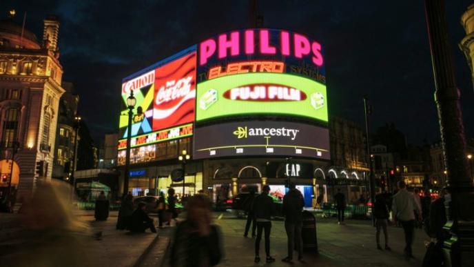 A photograph of Piccadilly Circus showing the outdoor marketing screens at nighttime.  