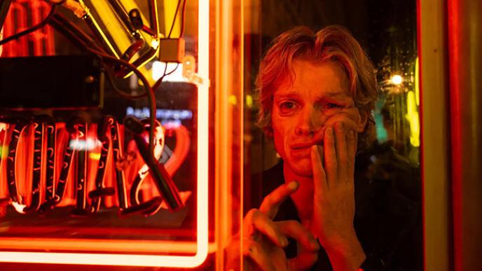 Matt Hagen looks at his reflection in a neon-lit window as his face begins to melt