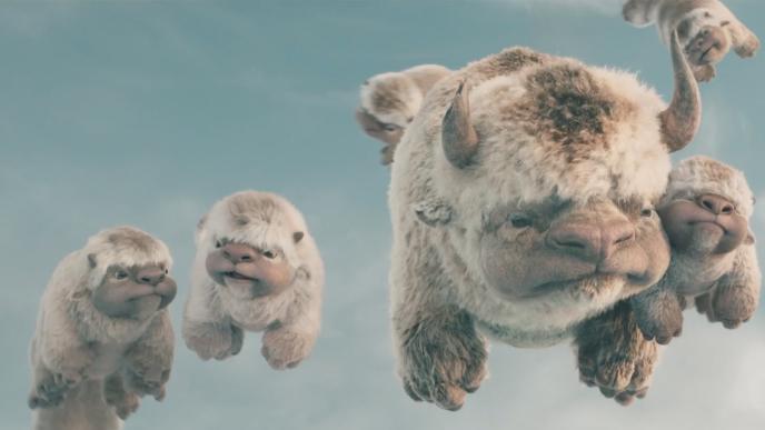 A large, CG animated furry, six-legged flying bison soars through the sky, surrounded by four fluffy, playful baby bison, also CG animated.