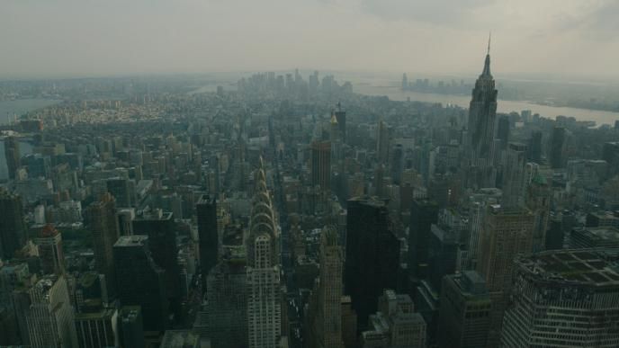 Aerial view of a destructed Manhattan’s skyline under hazy skies, featuring the Chrysler Building and Empire State Building.