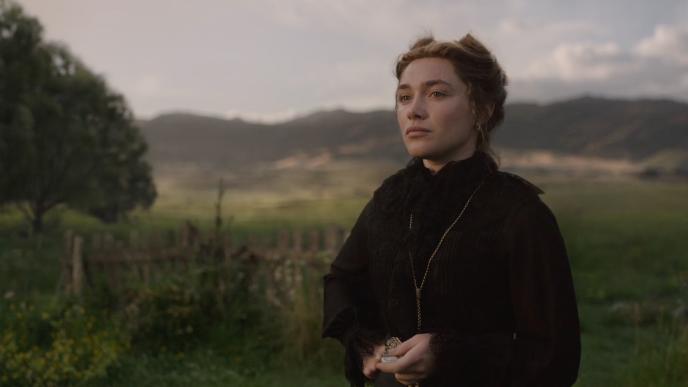 A solemn Cathy Ames (played by Florence Pugh) in Victorian black clothing stands in a grassy countryside, with rolling hills beneath a cloudy sky.