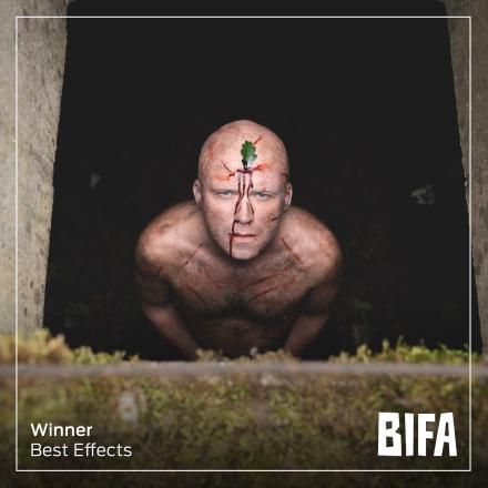 Rory Kinnear stares upwards, topless, with a leaf embedded in his forehead.